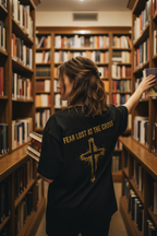 Frau in Bibliothek trägt schwarzes Fear Lost At The Cross Oversized T-Shirt mit goldenem Kreuz